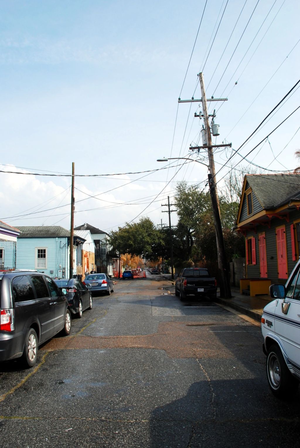 A New Orleans street with car park on both side. There is colored wooden house, and electric pole.
