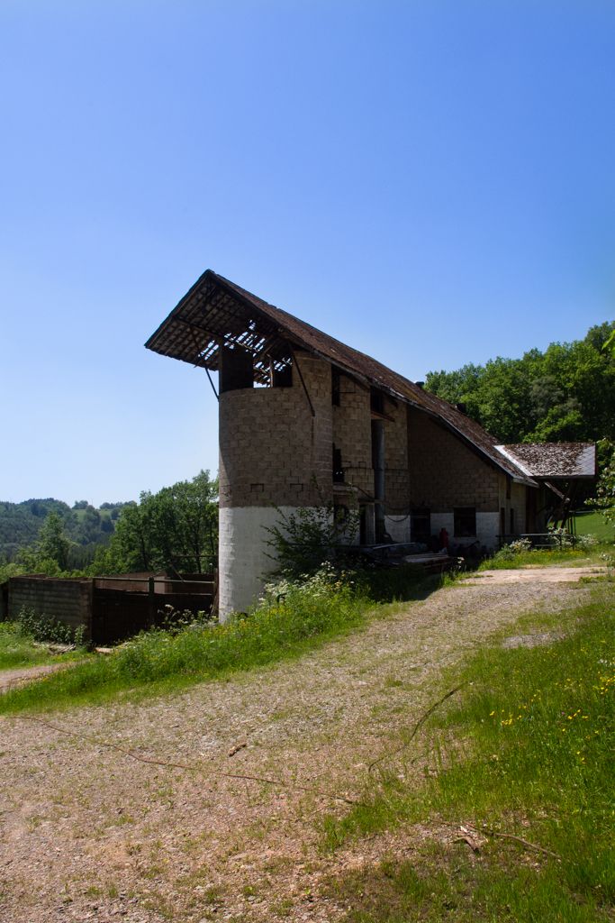 A ruined building, probably an ancient silo. In the background there are some forest. The weather is sunny.
