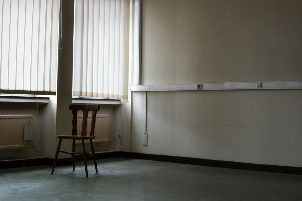 Inside an empty class room, a chair placed in front of windows with white blinds.