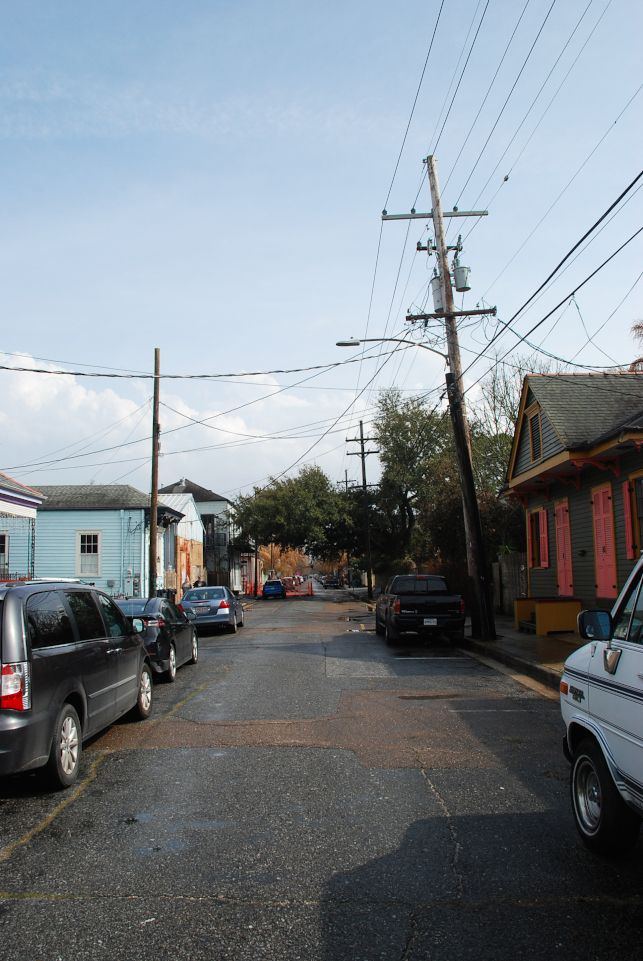 A New Orleans street with car park on both side. There is colored wooden house, and electric pole.
