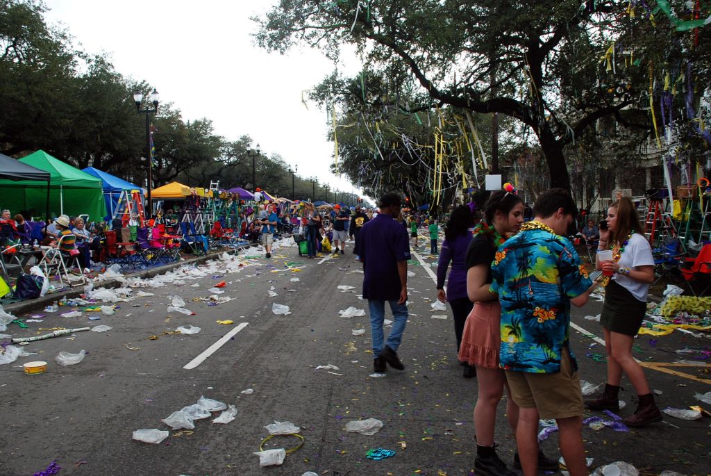 A street full of trash after a mardi-gras parade, some peoples are discussing.