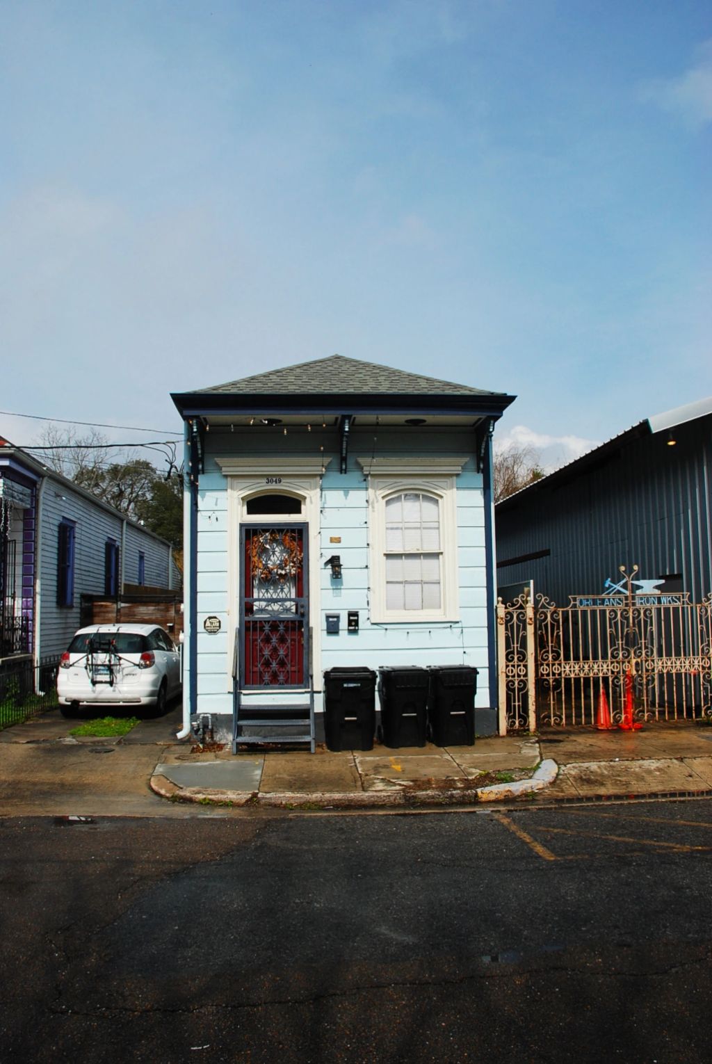 A New Orleans light blue shotgun house, with a car park in an alley.